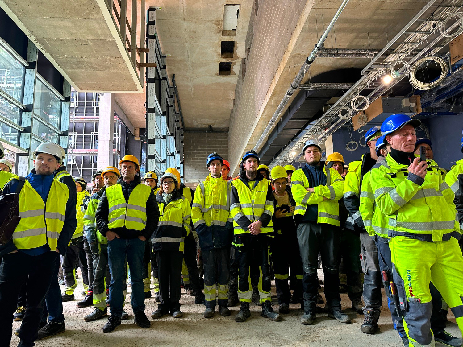 Būvniecības komanda ar ķiverēm un drošības vestēm sanāk uz apspriedi jaunbūvē