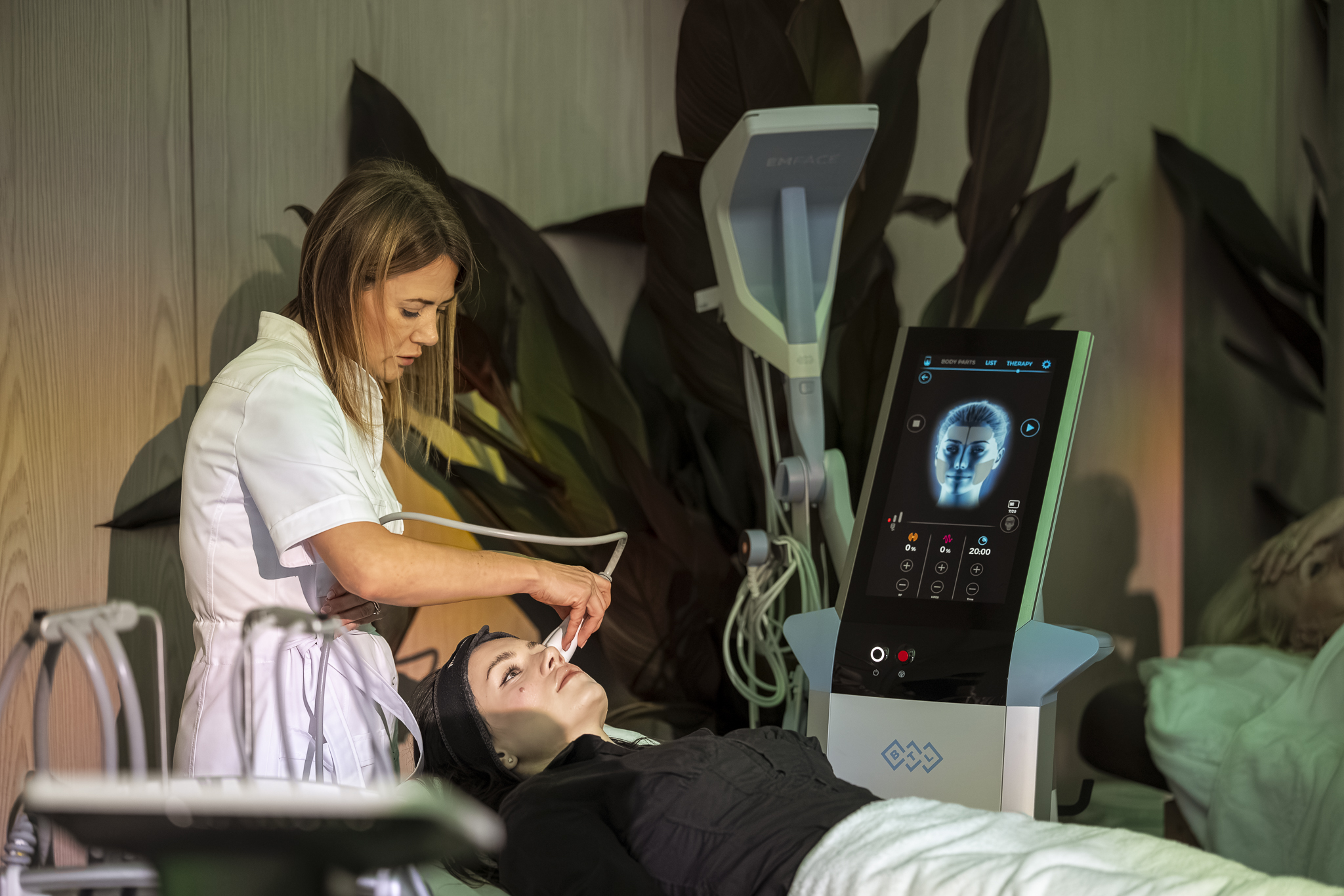 Kosmetoloģe veic sejas procedūru ar EMFACE aparātu veselības festivālā