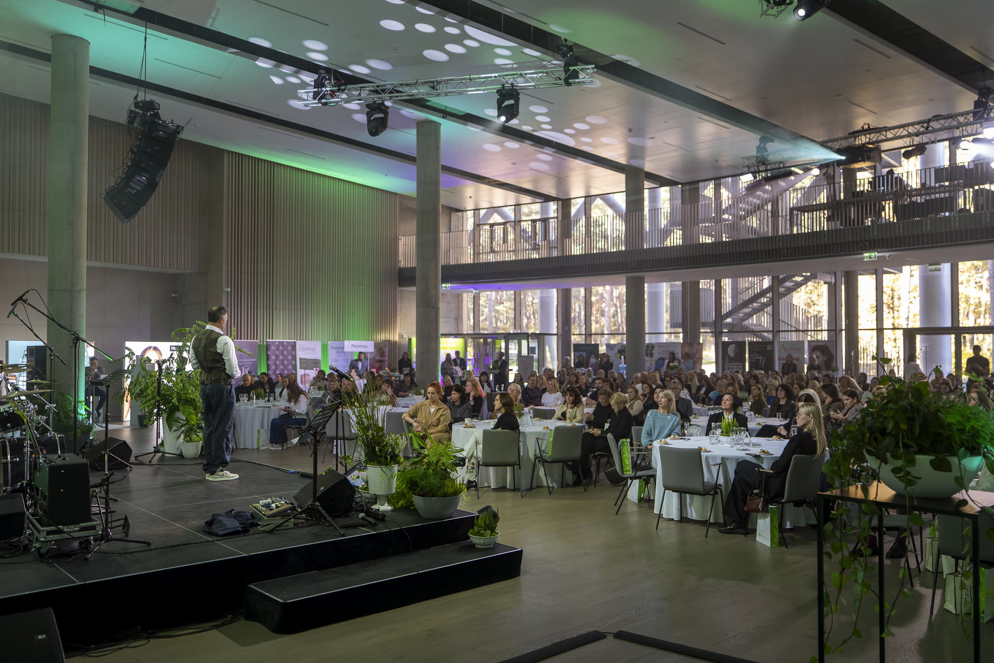 Runātājs uzstājas konferences zālē pilnas auditorijas priekšā  ✅ TITLE (title attribute):