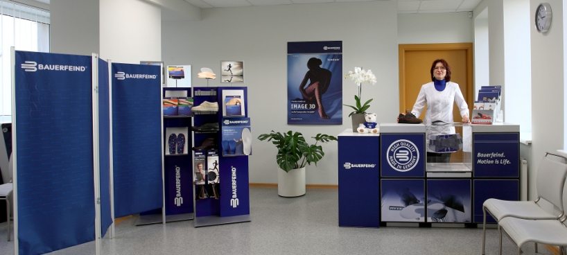 Bauerfeind ortopēdisko izstrādājumu telpa ar dažādiem atbalsta un kompresijas produktiem un konsultanti baltā ārsta halātā