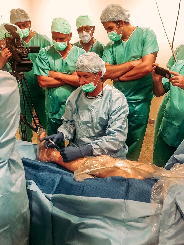 Ārsti vēro kolēģi, kurš veic vēnu ārstēšanas operācijas demonstrāciju